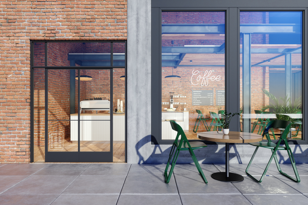 Store Window Of Coffee Shop With Table, Green Chairs In Front Of Shop And Brick Wall Background.